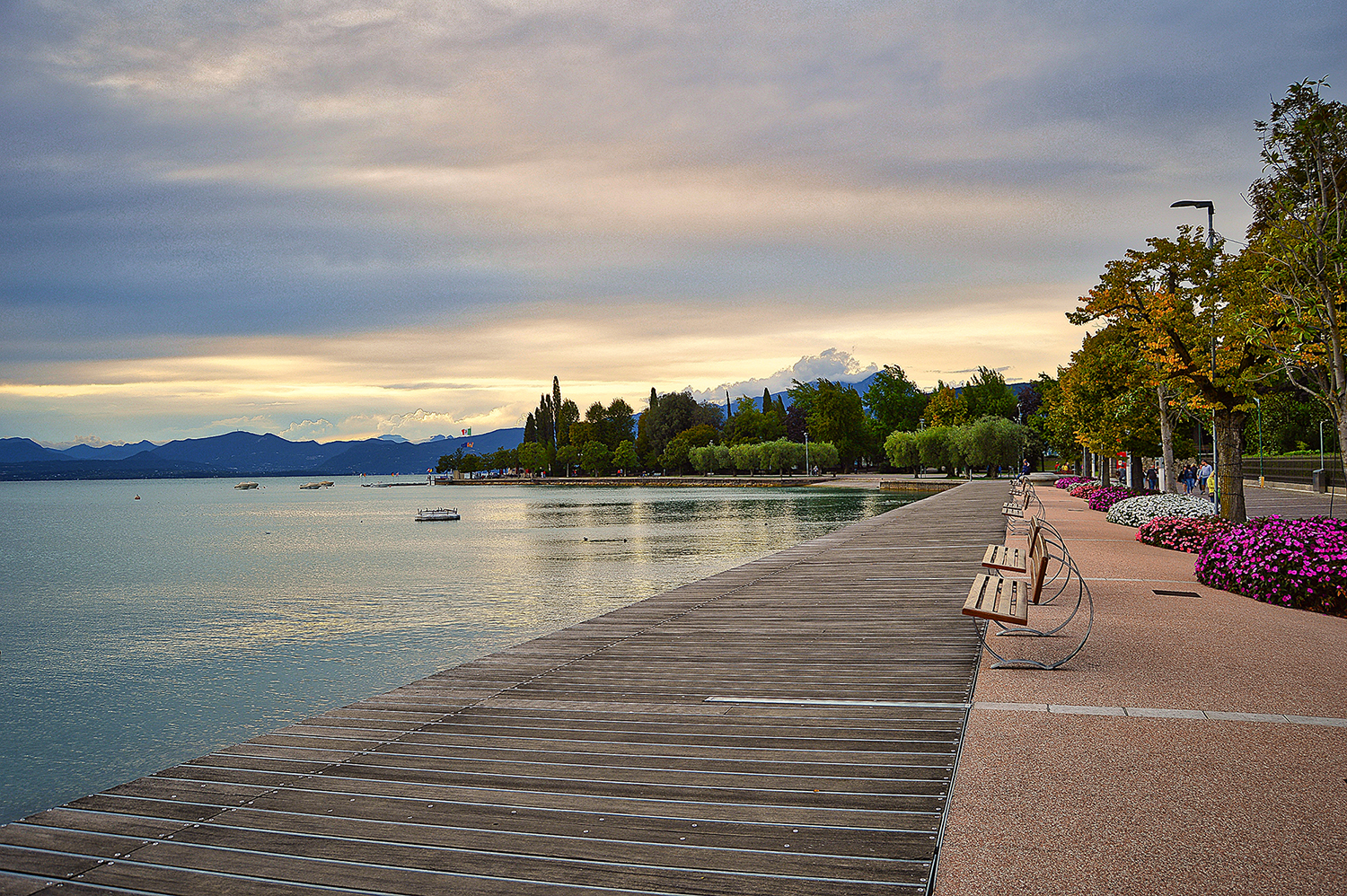 beautiful promenade pier of Bardolino, lake Garda. Landscape with benches, flowers, trees, water and dramatic evening sky